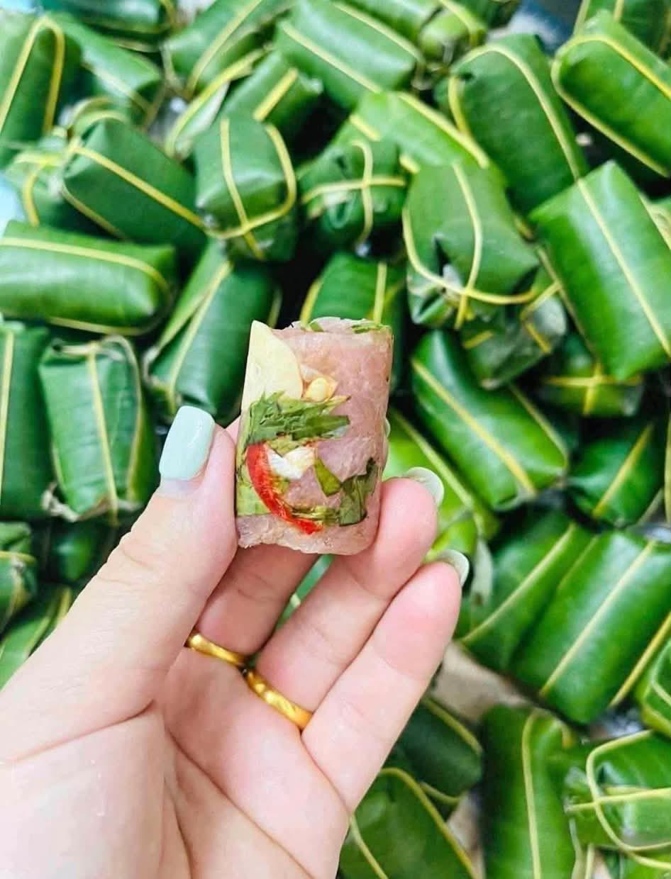 Chiếc nem chua đã bóc, thấy thịt nem màu hồng, tỏi, ớt và lá bên trong